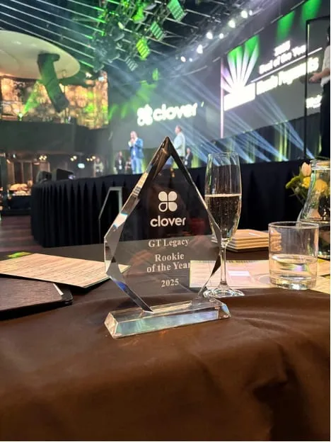 A glass Clover award engraved "GT Legacy — Rookie of the Year 2025", on a table at the conference.